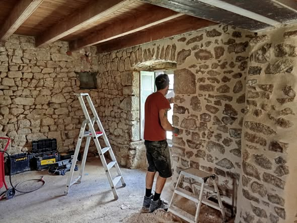 Travail de joints et finitions en cours sur un mur en pierre